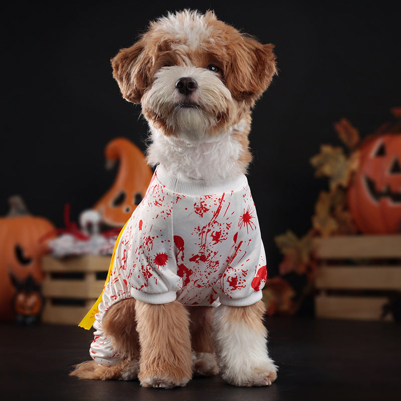 Dog wearing a Halloween-themed outfit with blood splatter design in front of pumpkins.