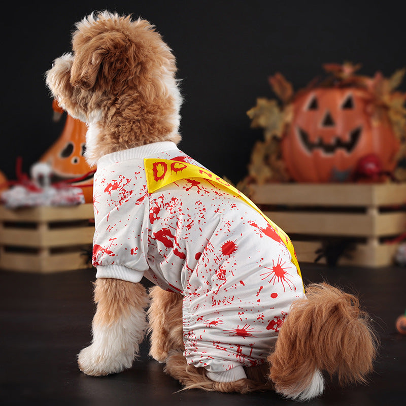 Dog wearing a Halloween-themed costume with blood splatters and a yellow 'DC' logo, standing in front of pumpkins.