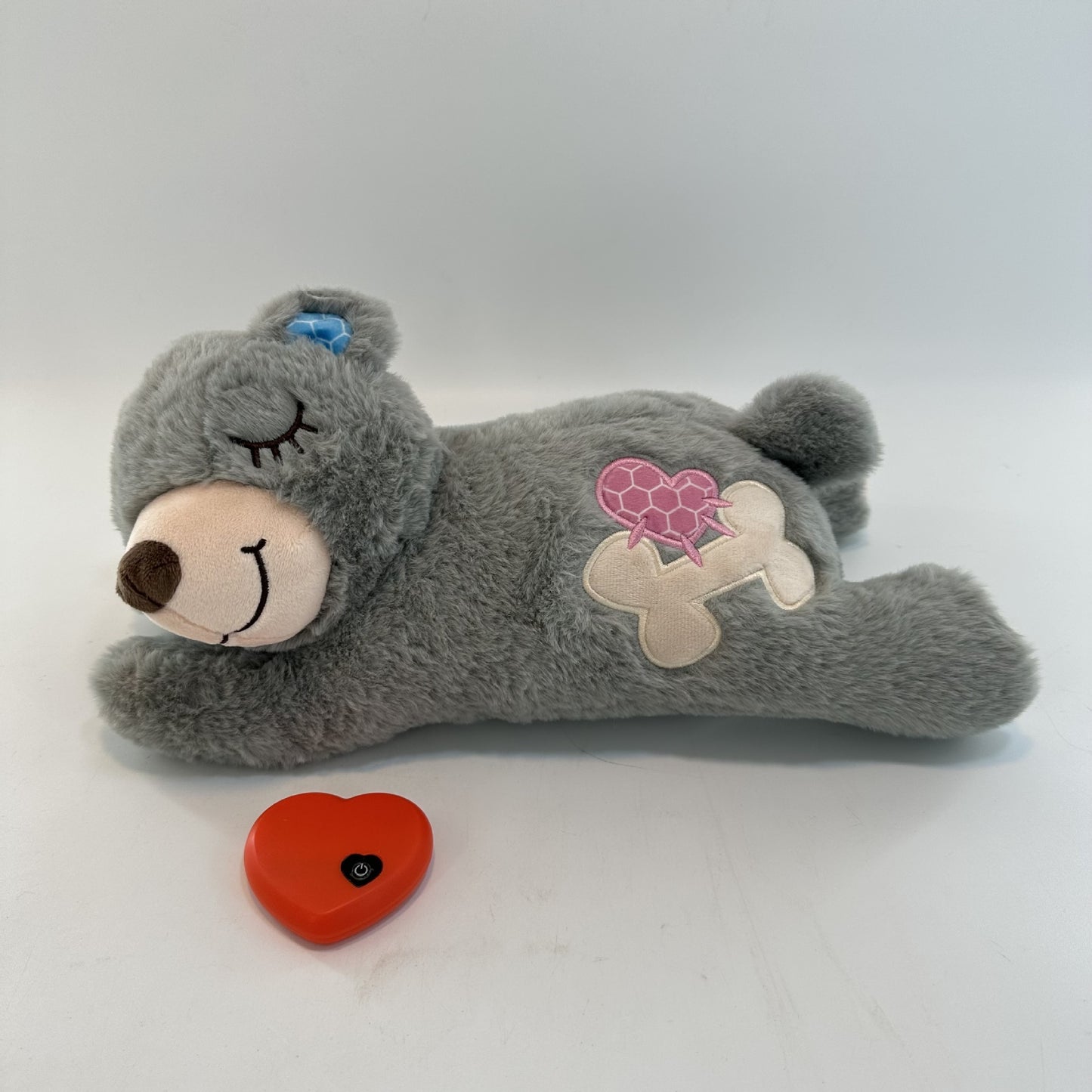 Gray teddy bear plush toy with heart and bone design on a white background