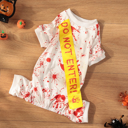White dress with red splatter design and yellow 'Do Not Enter!' sash on a wooden surface with Halloween decorations.