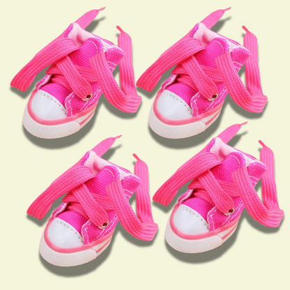 Small dog wearing four canvas sneakers, perfectly fitted on each paw, standing on a sidewalk — photorealistic image focused on pet shoes pink variant